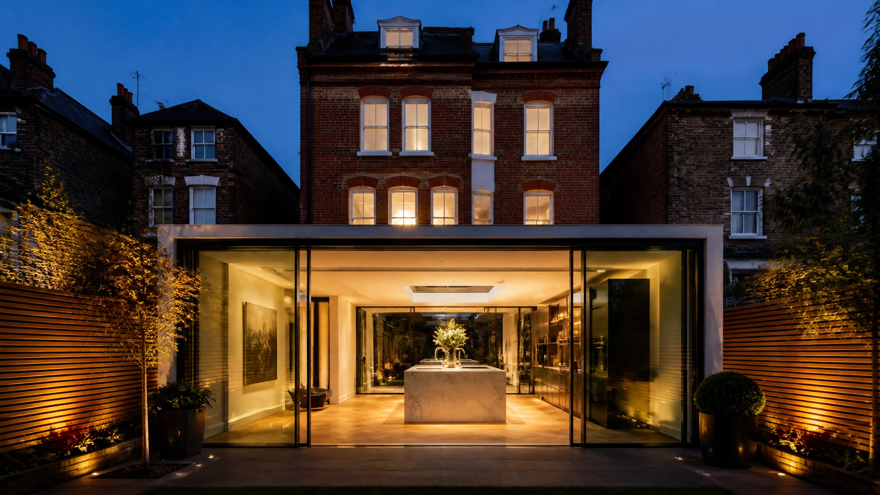 Luxury modern glass box extension on a Victorian red-brick house in Kensington at dusk
